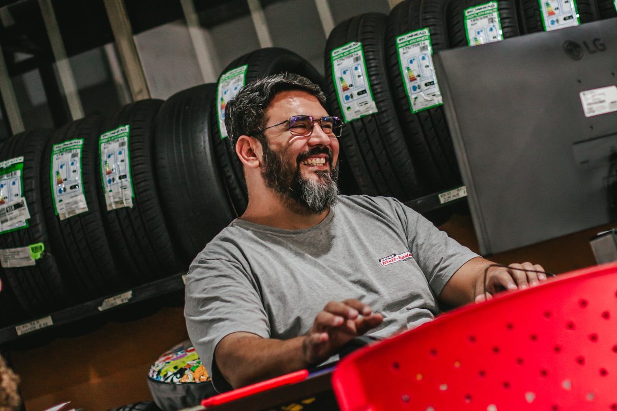 Cliente sorrindo na loja da Mult-Rodas, com estoque de pneus de várias marcas ao fundo
